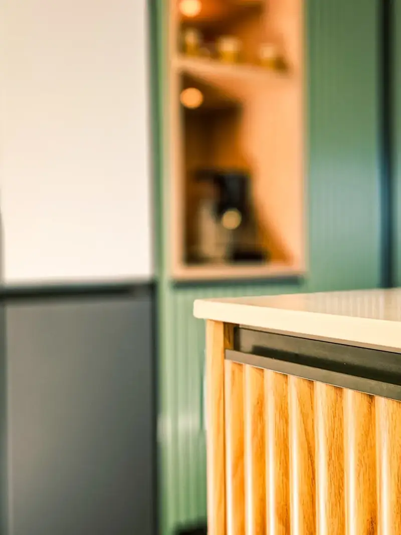Fluted timber detailing beside green kitchen cabinetry